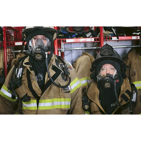 Two firefighters wearing Fire-Dex® Captain Jim Particulate Blocking Hoods, showing thermal and particulate protection while working together in a hazardous environment.