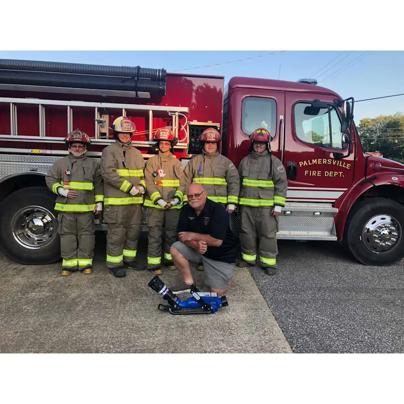 Five firefighters in tan Fire-Dex® turnouts and a kneeling man with a blue nozzle pose in front of a red Palmersville Fire Dept. truck.