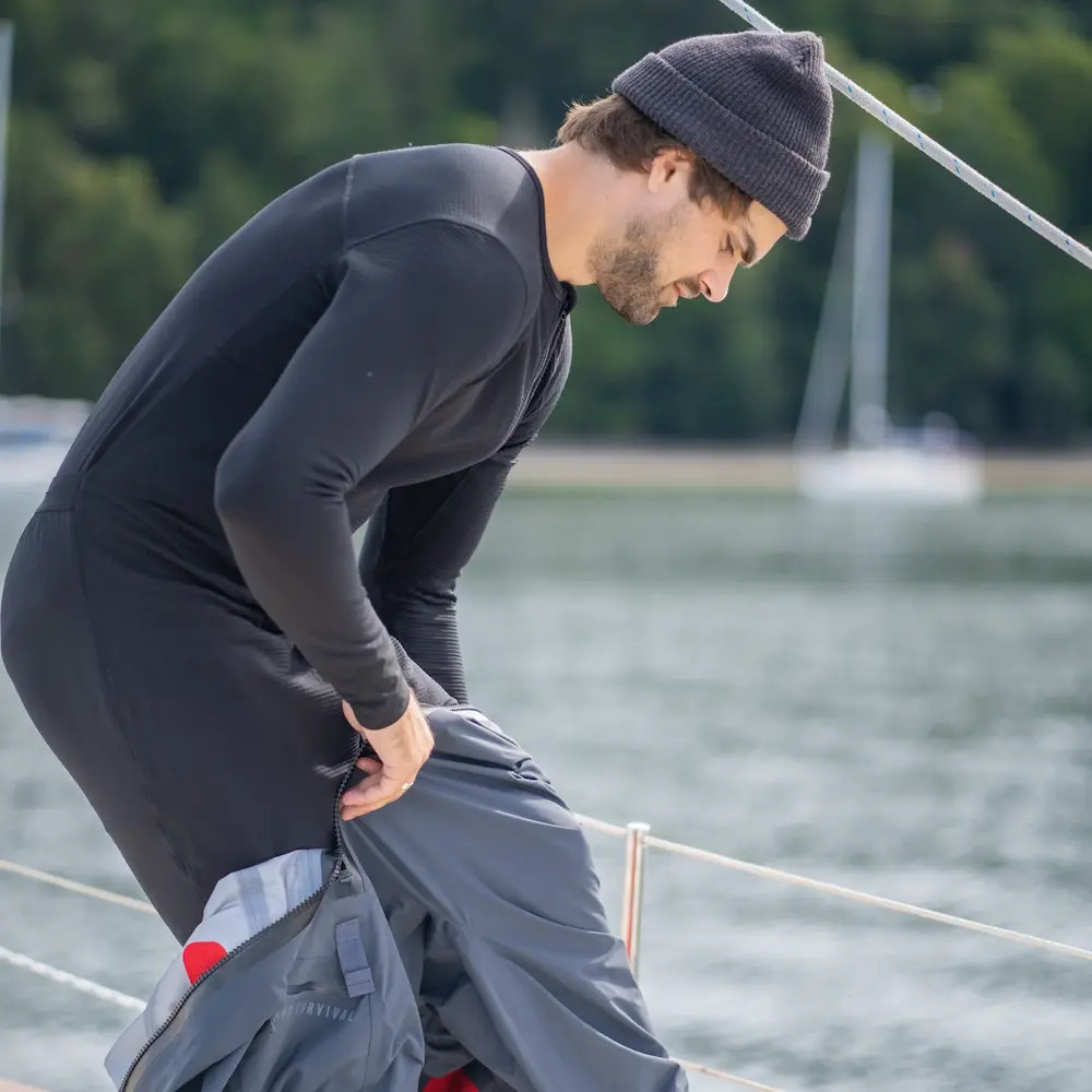Man pulling on the pants of a dry suit while wearing a Mustang Survival® Men’s Kazan Dry Suit Liner for thermal protection and comfort.