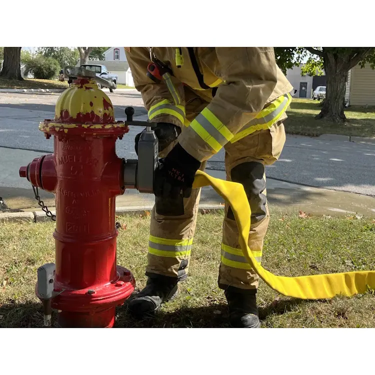 Firefighter attaching the BullDog™ Ultima™ yellow firefighting hose to a fire hydrant, demonstrating quick-connect capabilities and robust hose design for emergency use.