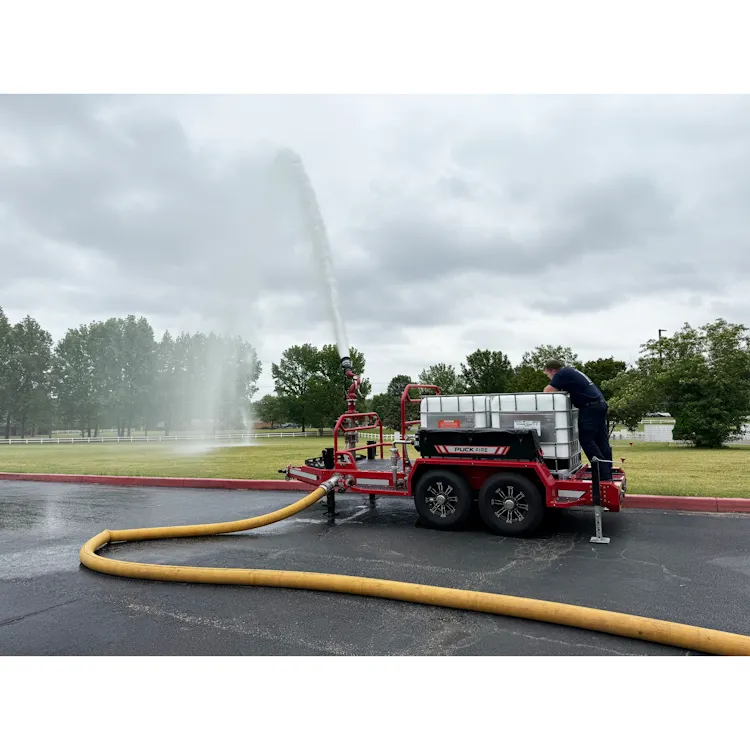 Yellow BullDog™ Hi-Vol® firefighting hose supplying a trailer-mounted water monitor spraying a tall stream of water across a parking lot.