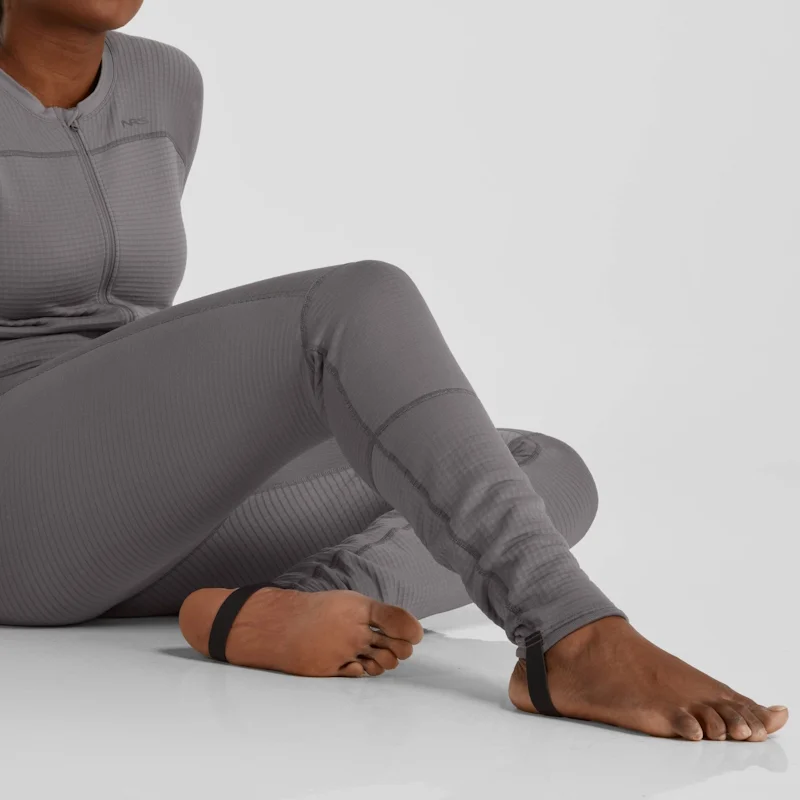Closeup of a woman sitting on the ground wearing the NRS Women’s Lightweight Union Suit, focusing on the leg area to showcase the soft, stretchy fabric and full-length design.