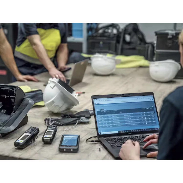 Workers at a table with hard hats, a docking station, a laptop displaying data management software, and Dräger X-am® 2800 Multi-Gas Detectors.