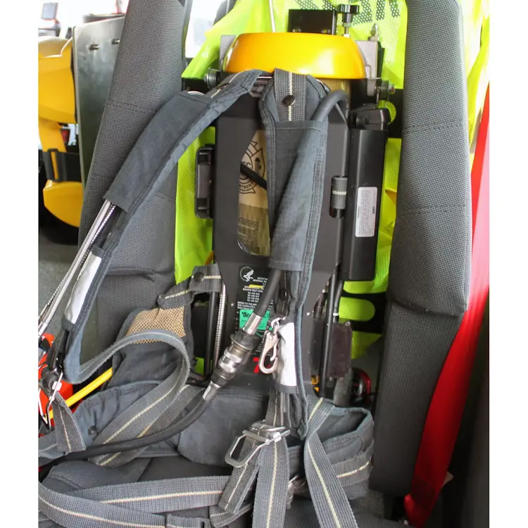 Close-up of an empty Ziamatic™ EZ-LOC Mechanical Bracket with Fixed Top Clamp mounted on a firetruck seat, featuring attached shoulder carrying straps and ready to securely hold a cylinder during emergencies.