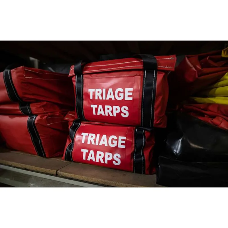 Red Husky® Triage Tarps carry bags stacked on a storage shelf beside folded red, yellow, and black Husky® emergency equipment staging mats.