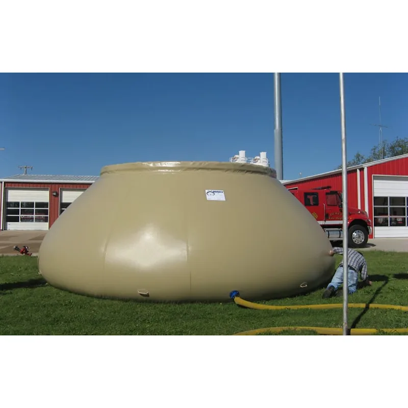 Large tan Husky® self-supporting frameless portable water tank on a lawn at a fire station, connected to a yellow hose with a person kneeling beside it.