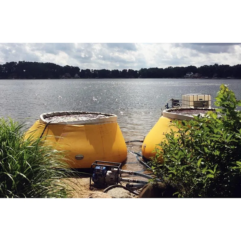 Two yellow Husky® self-supporting frameless portable water tanks filled with water on a lakeshore with a portable pump and hoses in the foreground.