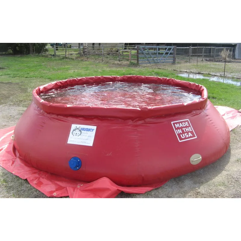 Red Husky® self-supporting frameless portable water tank filled with water on a red ground tarp, with a "Made in the USA" label and blue side outlet.