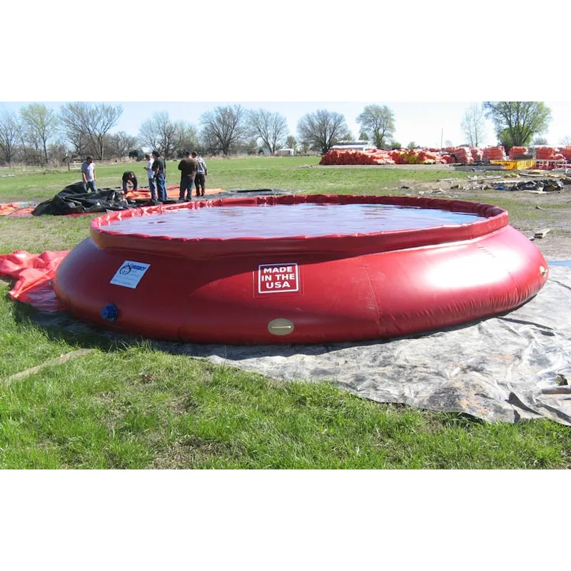Large red Husky® self-supporting frameless portable water tank filled with water on a gray ground tarp in a grassy field, with a "Made in the USA" label and people standing in the background.