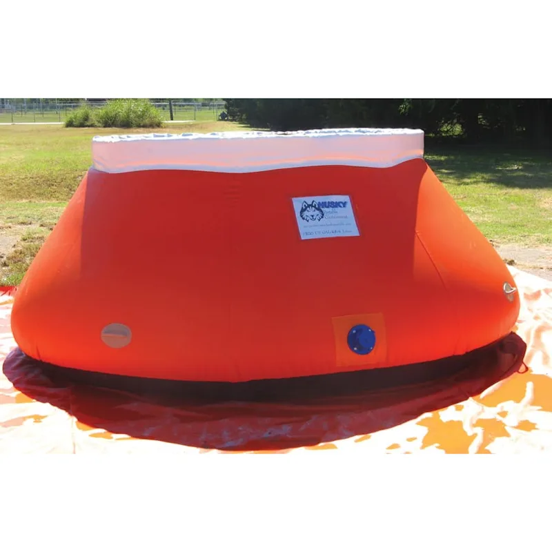 Orange Husky® self-supporting frameless portable water tank with white upper collar, blue side outlet, and side fittings on a ground tarp in a grassy area.
