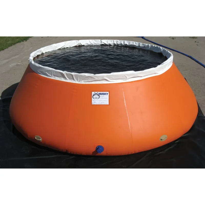 Orange Husky® self-supporting frameless portable water tank filled with water on a black ground tarp, with white upper collar and side fittings.