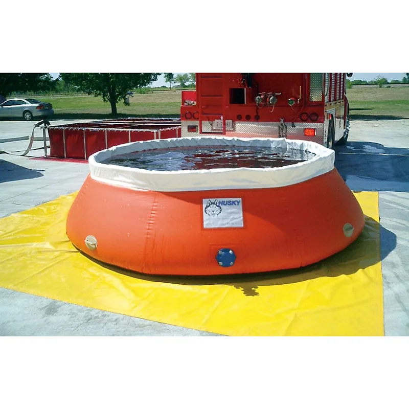 Orange Husky® self-supporting frameless portable water tank filled with water on a yellow ground tarp beside a fire truck and a frame-style folding tank.