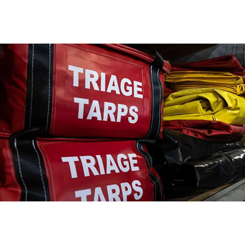 Stacked red Husky® Triage Tarps bags next to folded yellow, red, and black Husky® emergency equipment staging mats on a storage shelf.