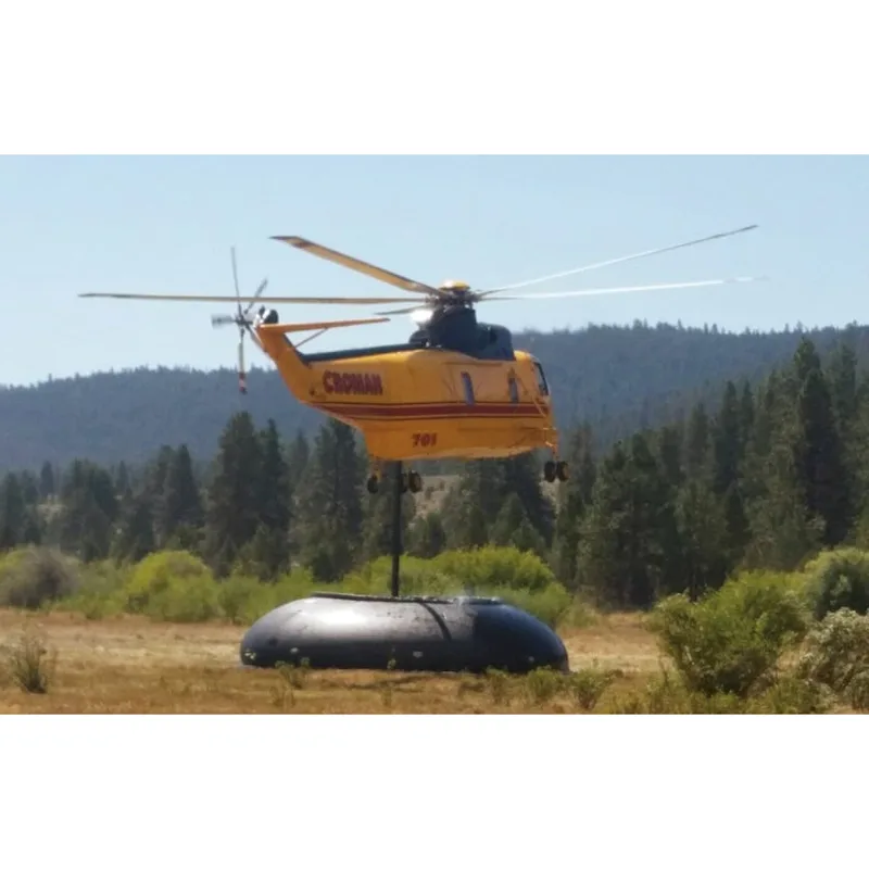 Yellow helicopter hovering over a black Husky® self-supporting frameless portable water tank in a grassy field with a forested hillside behind.