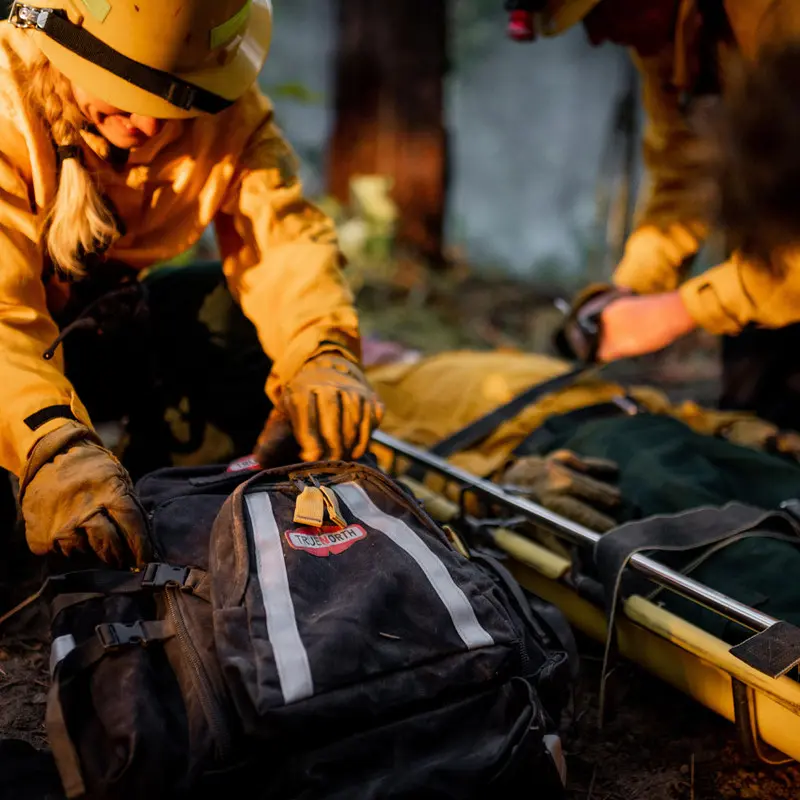 Firefighter laying down the True North Gear Firefly™ Medic Pack, ready to open it, highlighting its durable construction and organized design for quick access to medical supplies in emergency situations.