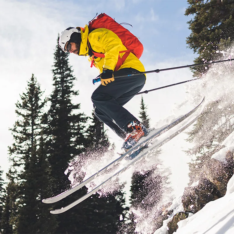 Skier wearing Team Wendy® M-216™ Ski Helmet in red/gray airborne while going down a snowy slope, demonstrating lightweight, durable, and high-performance winter protection.