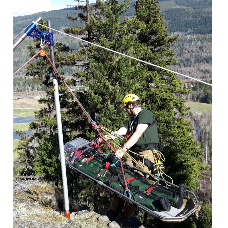 Side view of the Ruth Lee™ Working at Height Training Manikin being lifted on a stretcher outdoors, showcasing coordinated rescue efforts and safe rigging techniques in an open-air training environment.