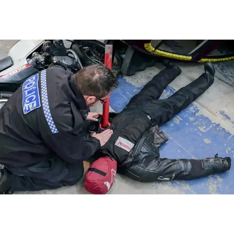 Ruth Lee™ Multi Trauma Training Manikin lying on the ground with simulated impalement injuries while a police officer inspects it during a training exercise.