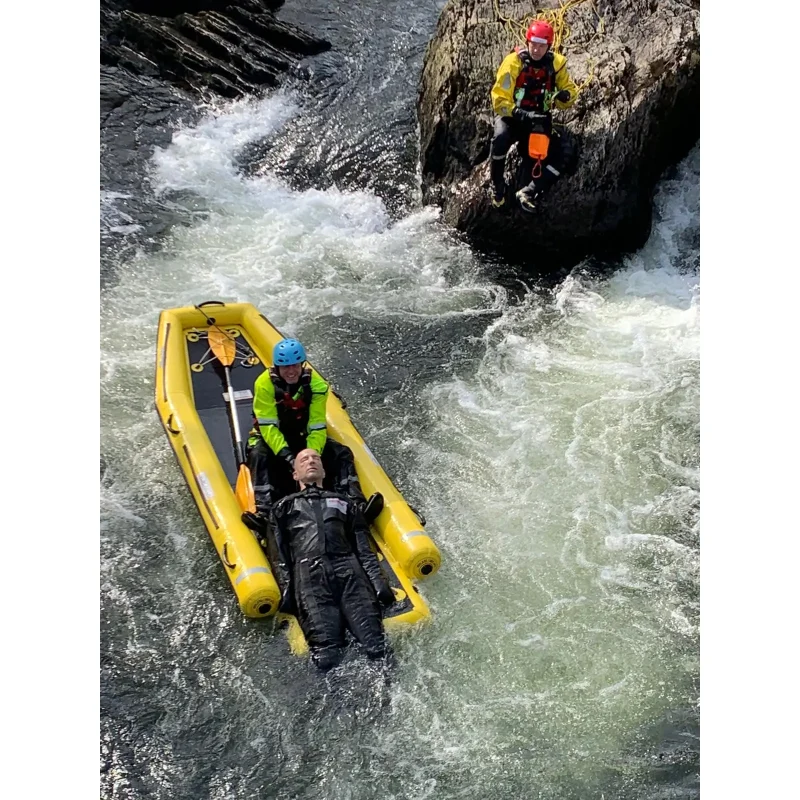 A Ruth Lee™ Advanced Water Rescue Manikin being carried onto a raft by rescue personnel in a white water river during an emergency water rescue training exercise.