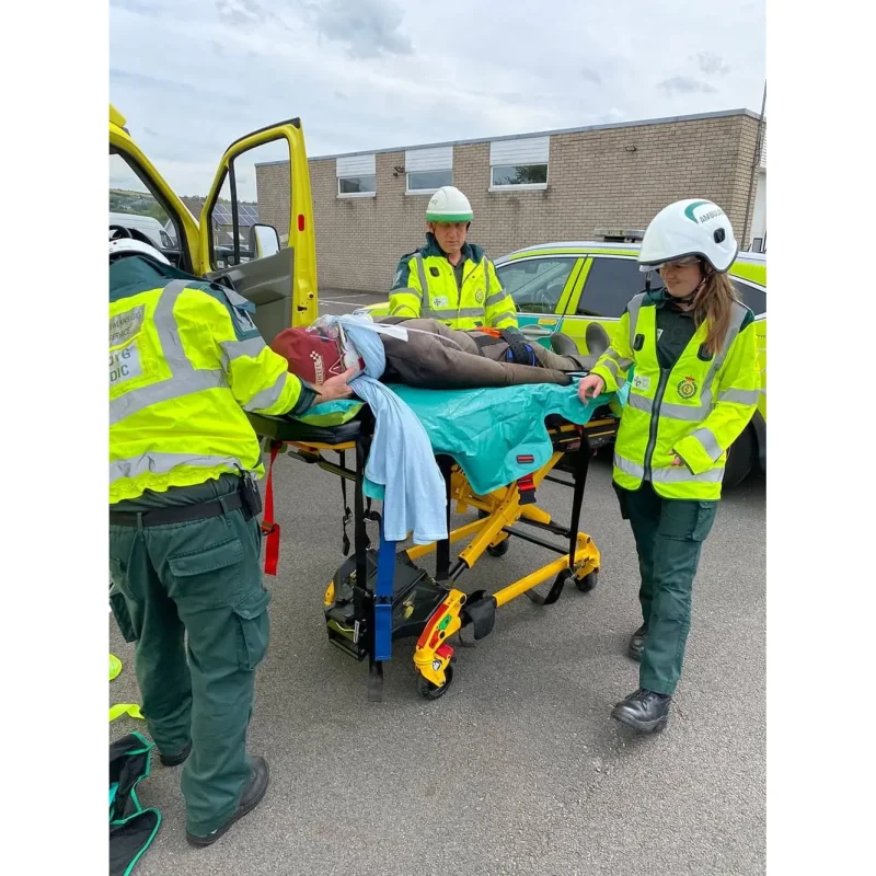 A Ruth Lee™ Duty Training Manikin lies on a stretcher cart being moved by rescue personnel during an emergency training exercise.