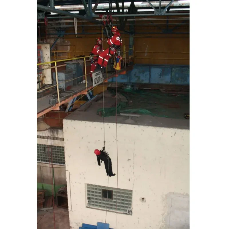 Distant shot of a Ruth Lee™ Working at Height Training Manikin being lifted by a rescue crew inside a warehouse, showcasing indoor high-angle rescue training and team coordination in an industrial environment.