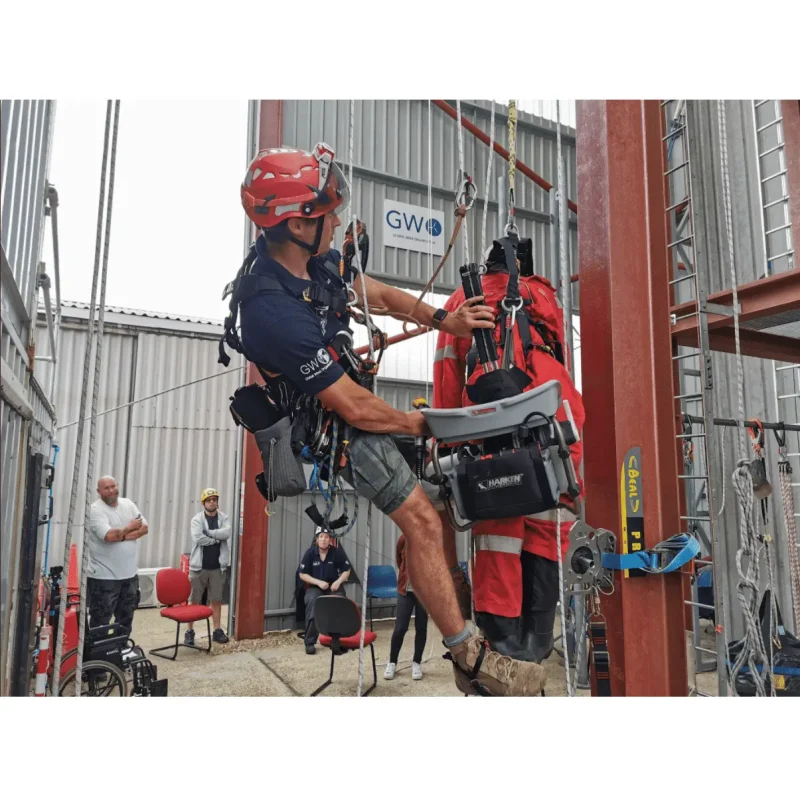 Ruth Lee™ Working at Height Training Manikin held by a rescue trainer near the ground while still hooked up to lifting equipment, demonstrating hands-on instruction and safety procedures during high-angle rescue training.