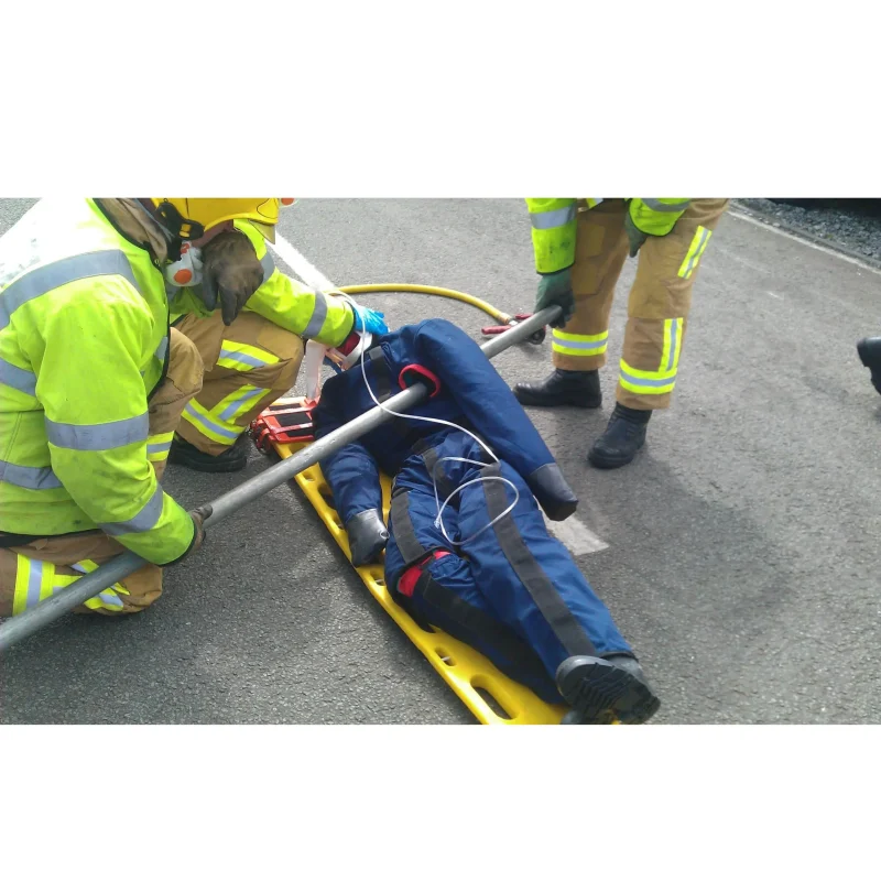 A Ruth Lee™ Multi Trauma Training Manikin with visible impalement injuries lying on a stretcher, used in a simulated emergency trauma care and evacuation training scenario.