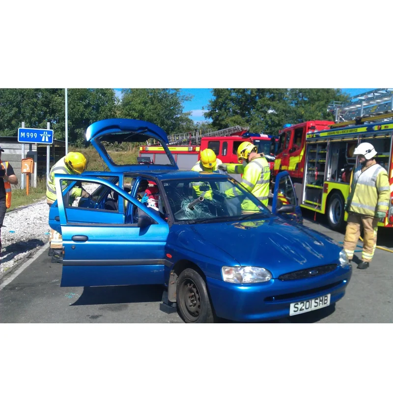 A wider view showing a Ruth Lee™ Multi Trauma Training Manikin with impalement injuries positioned in the front passenger seat of a car, as part of a realistic vehicle extrication and emergency trauma training scenario.